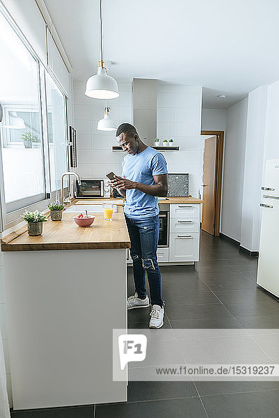 Young man using cell phone in kitchen at home