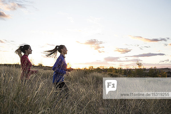 Junge Frauen rennen bei Sonnenaufgang gemeinsam über eine Wiese