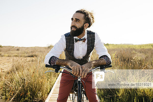 Gut gekleideter Mann mit seinem Fahrrad auf einem Holzsteg auf dem Land  der eine Pause macht
