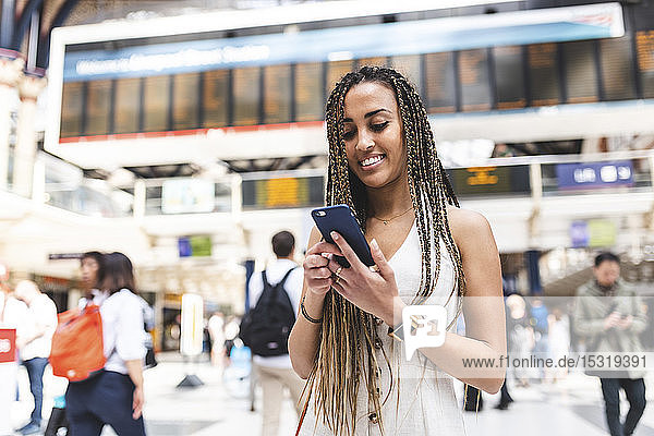 Portrait of happy young woman at train station using smartphone  London  UK