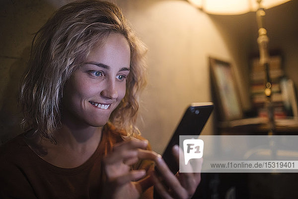 Porträt einer jungen Frau  die zu Hause ein Smartphone benutzt
