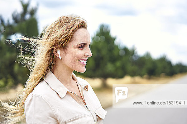 Porträt einer glücklichen Frau mit drahtlosen Kopfhörern in der Natur