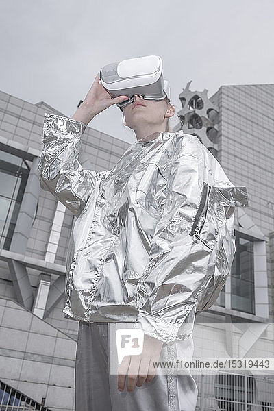 Girl in silver suit. looking through VR goggles in futuristic city