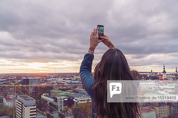 Frau  die vor Sonnenuntergang mit einem Smartphone von einer Aussichtsterrasse aus ein Foto macht  Tallinn  Estland