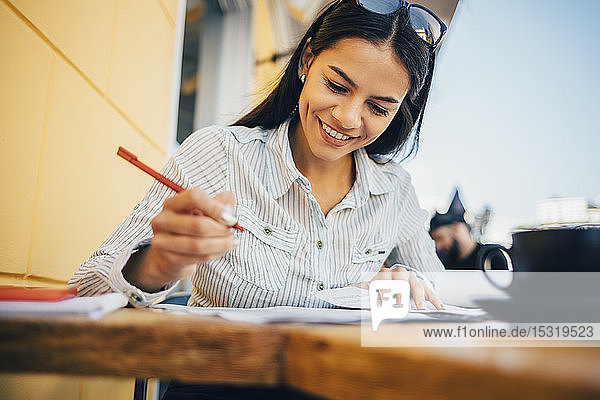 Lächelnde junge Frau macht Notizen in einem Cafe