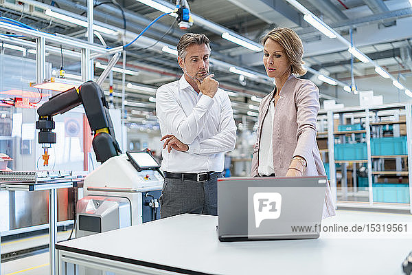 Businessman and businesswoman with laptop talking in a modern factory hall