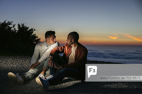 Schwules Paar sitzt bei Sonnenuntergang in den Bergen über den Wolken