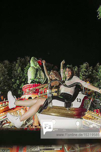 Two excited young women in a fairground ride on a funfair at night