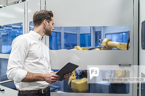 Businessman with tablet looking at robot in a modern factory