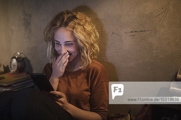 Porträt einer überraschten jungen Frau  die zu Hause ein Smartphone betrachtet