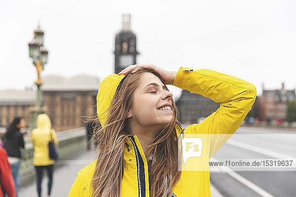 Happy young woman wearing yellow raincoat on a rainy day  London  UK