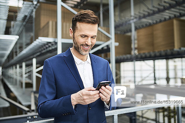 Smiling businessman using cell phone in a factory