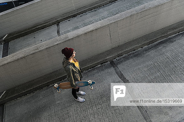 Stylish young woman with skateboard standing on parking deck