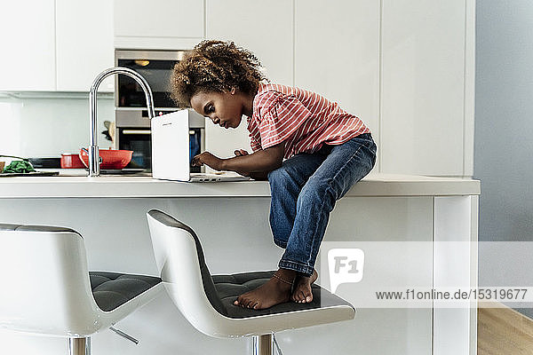 Girl sitting on kitchen counter using laptop