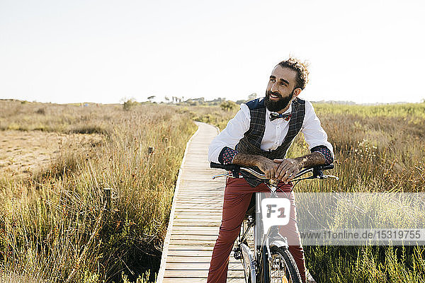 Well dressed man with his bike on a wooden walkway in the countryside having a break