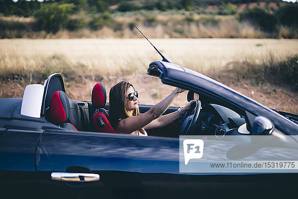 Junge Frau mit Sonnenbrille  die in ihrem Cabrio sitzt