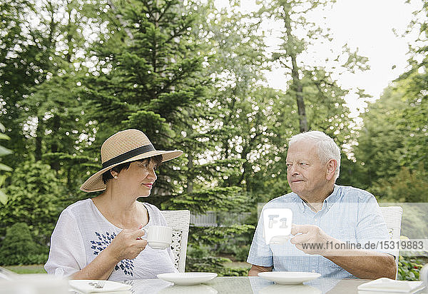Älteres Ehepaar trinkt Kaffee im Garten und sieht sich gegenseitig an