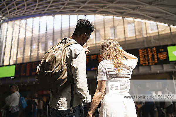 Rückansicht eines jungen Paares mit Blick auf die Anzeigetafel des Bahnhofs  London  UK