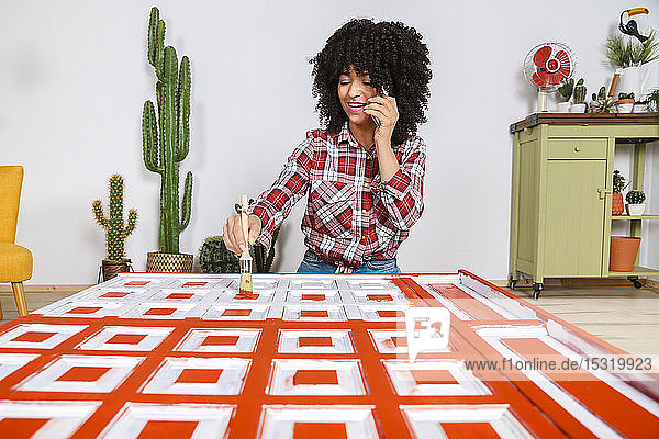 Frau malt Möbel mit Pinsel und benutzt Smartphone zu Hause
