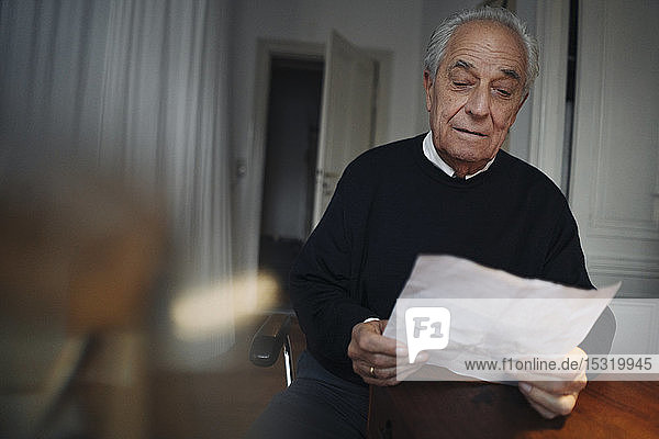 Älterer Mann sitzt zu Hause am Tisch und liest eine Zeitung