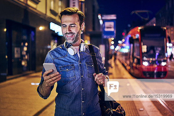 Lächelnder Mann benutzt nachts in der Stadt sein Smartphone