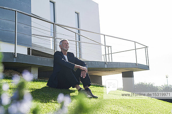 Leitender Geschäftsmann sitzt auf dem Rasen vor einem Gebäude