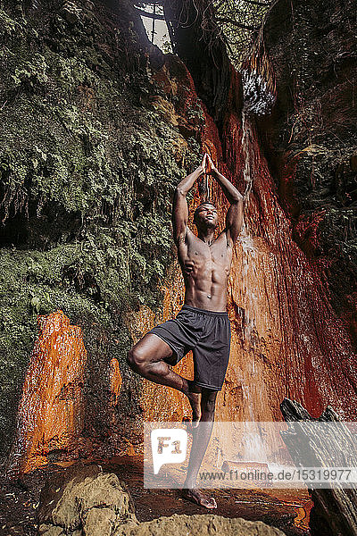 Yoga praktizierender Mann am Wasserfall  Baumposition