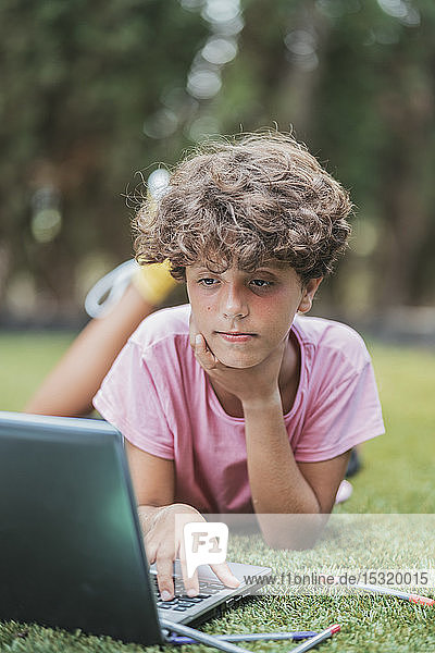 Junge liegt mit Laptop im Gras