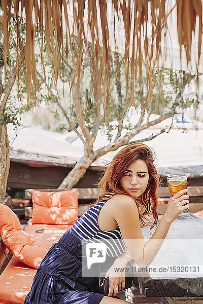 Junge Frau mit einem Getränk  die auf einer Bank im Freien sitzt und sich umsieht