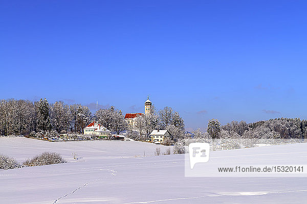 Pfarrkirche St. Johann Baptist in schneebedeckter Landschaft vor strahlend blauem Himmel