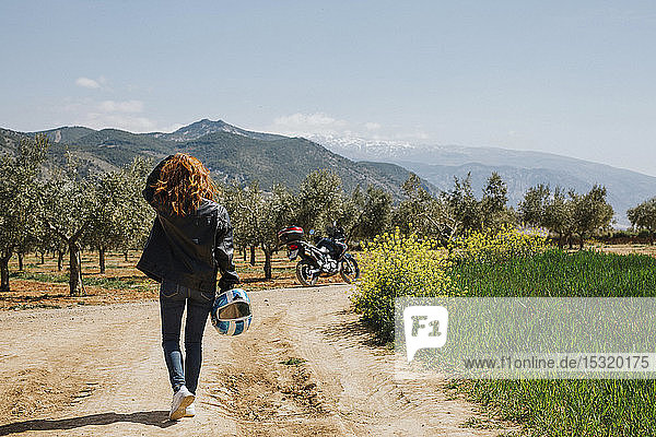 Back view of redheaded motorcyclist walking on dirt track  Andalusia  Spain
