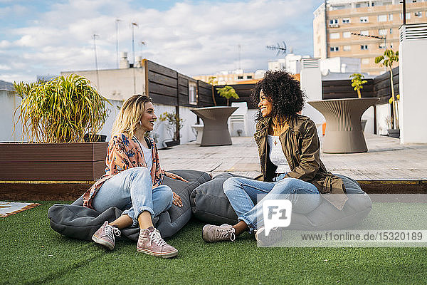 Multikulturelle Frauen unterhalten sich auf Kissen sitzend auf einer Terrasse