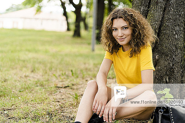 Porträt einer lächelnden jungen Frau  die in einem Park sitzt