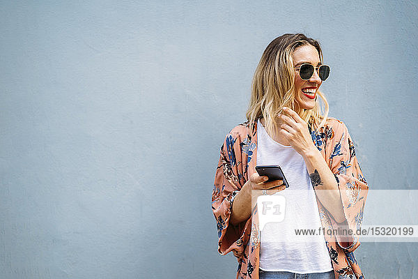 Lächelnde blonde Frau mit Smartphone  blauer Hintergrund