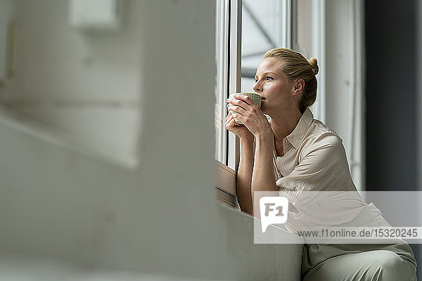 Junge Geschäftsfrau mit einer Tasse Kaffee  die aus dem Fenster schaut