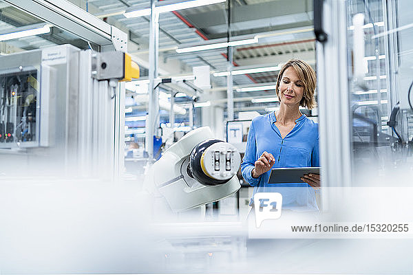 Geschäftsfrau mit Tablette am Montageroboter in einer Fabrik