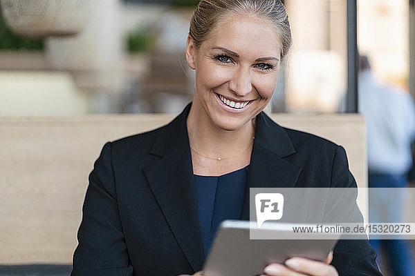 Porträt einer lächelnden blonden Geschäftsfrau mit digitalem Tablet in einem Café