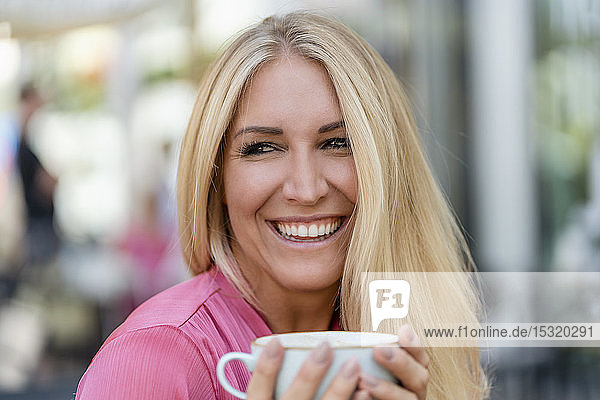 Porträt einer glücklichen blonden Frau mit einer Tasse Kaffee