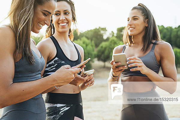 Three happy sportswomen using smartphones after workout