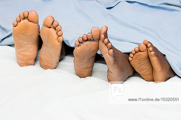 diese Familie liegt im Bett und zeigt ihre nackten Füße und halb zugedeckt