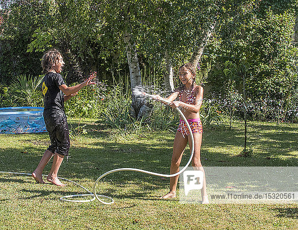 Zwei Jungen im Alter von 4 und 12 Jahren und ein zehnjähriges Mädchen spielen mit einem Schlauch im Garten