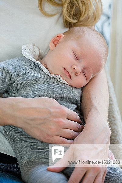 Ein 2 Monate altes Baby schläft in den Armen seiner Mutter.
