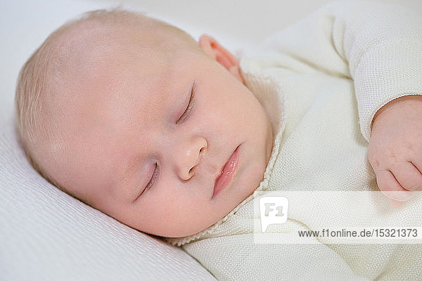 Nahaufnahme eines kleinen Säuglings in weißer Kleidung von 2 Monaten  der auf einem weißen Bett schläft.