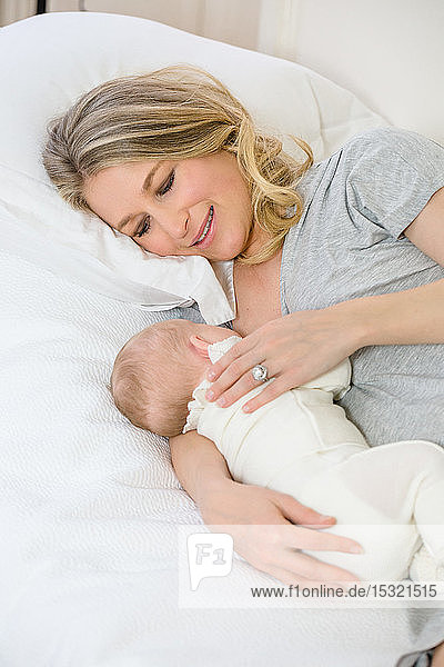 Porträt einer schönen jungen lächelnden Mutter  die ihrem Baby die Brust gibt.