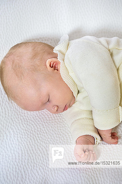 Nahaufnahme eines kleinen Säuglings in weißer Kleidung von 2 Monaten  der auf einem weißen Bett schläft.
