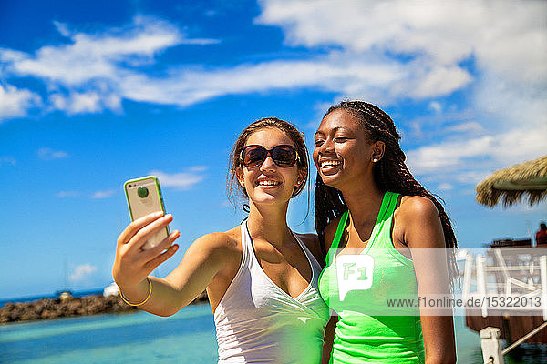 2 smiling girls taking a selfie against blue sky background.