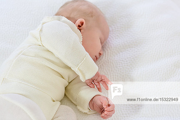 Kleiner Säugling in weißer Kleidung von 2 Monaten schläft auf einem weißen Bett.