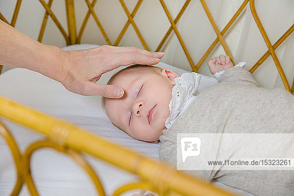 Hand einer Mutter auf dem Kopf ihres 2 Monate alten Babys  das auf dem Rücken im Bett schläft.