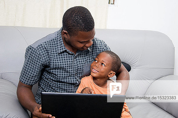Der Vater freut sich  dass sein Kind einen Laptop kennenlernt und mit ihm arbeitet.