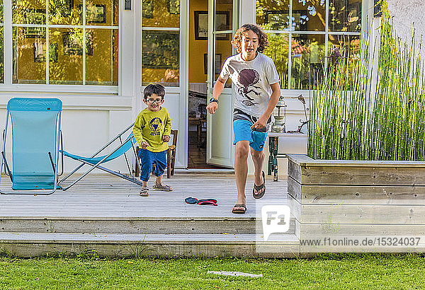 Zwei Jungen im Alter von fünf und dreizehn Jahren rennen aus dem Haus in Richtung Garten